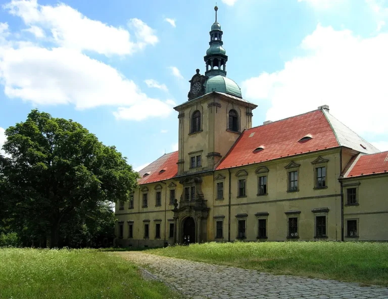 Klášterní budovy v Oseku s věží kostela za zelenou loukou