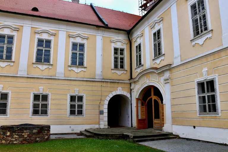 Žluté a bílé fasády kláštera v Nové Říši kolem nádvoří s obloukovými vstupy
