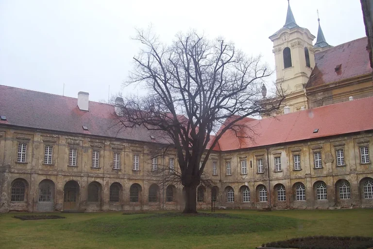 Rajský dvůr kláštera v Rajhradě s arkádami, červenými střechami a stromem bez listí