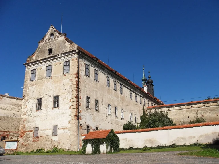 Nároží zámecké budovy v Uherčicích s omítkou, červenými střechami a navazující zdí