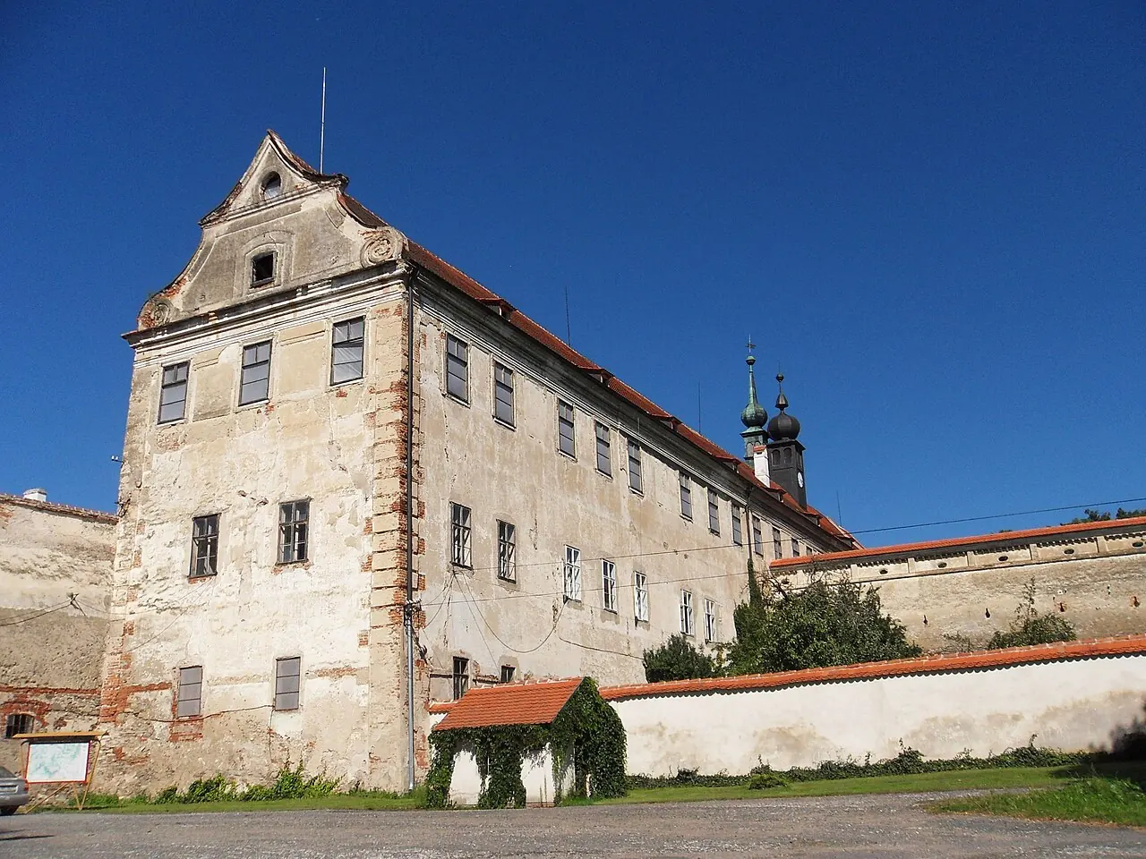 Nároží zámecké budovy v Uherčicích s omítkou, červenými střechami a navazující zdí