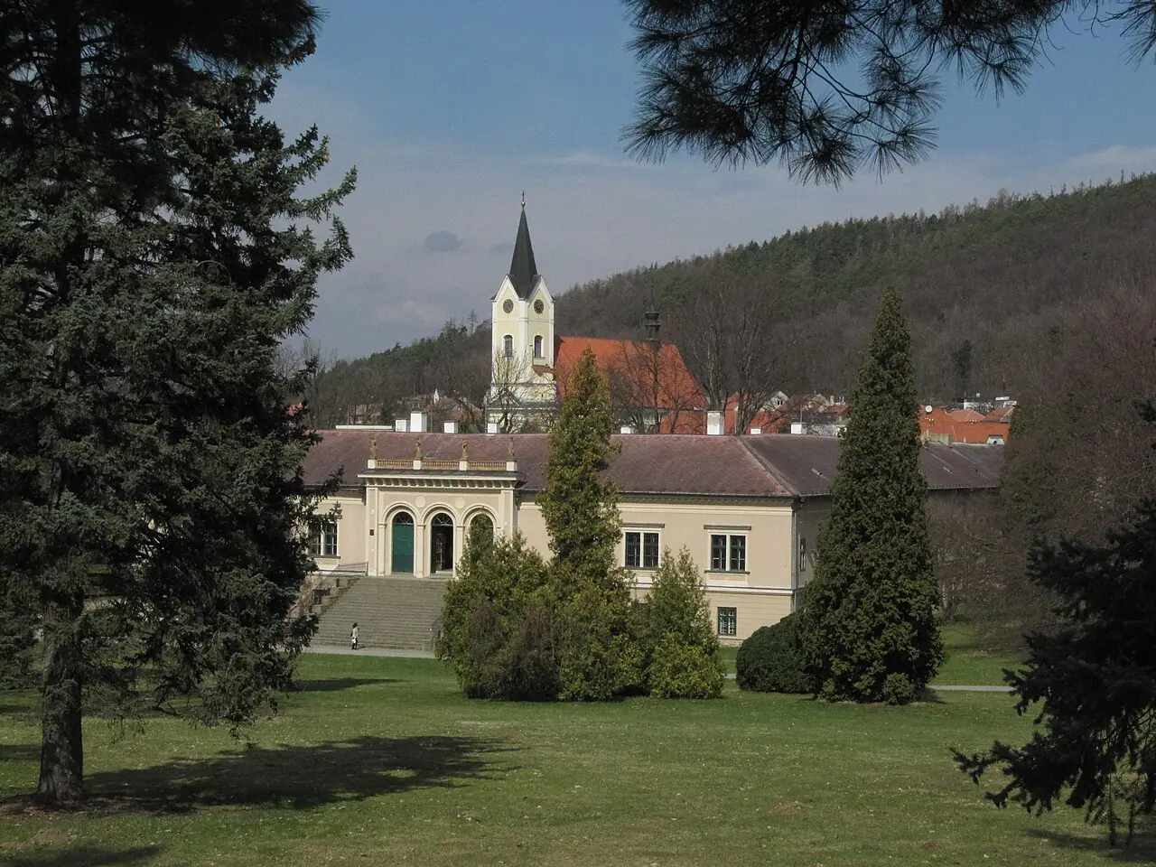 Pohled přes trávník a stromy parku na zámek v Čechách pod Kosířem s kostelní věží v pozadí