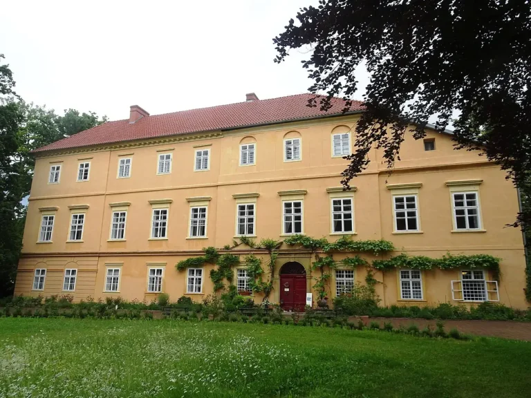 Žlutá patrová budova zámku Maleč s červenou střechou, okny a trávníkem před průčelím