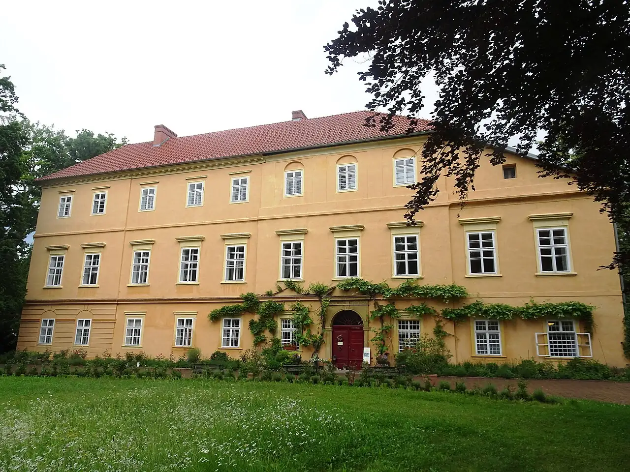 Žlutá patrová budova zámku Maleč s červenou střechou, okny a trávníkem před průčelím