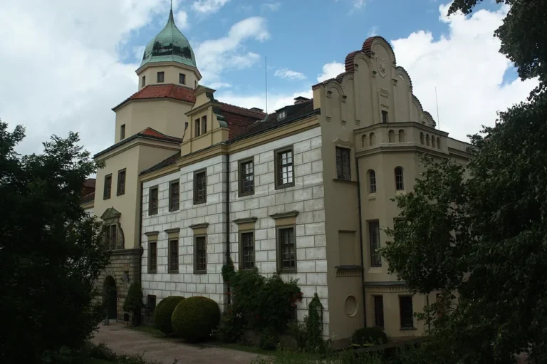 Světlé průčelí zámku Častolovice s vysokými okny, štíty a věží se zelenou střechou