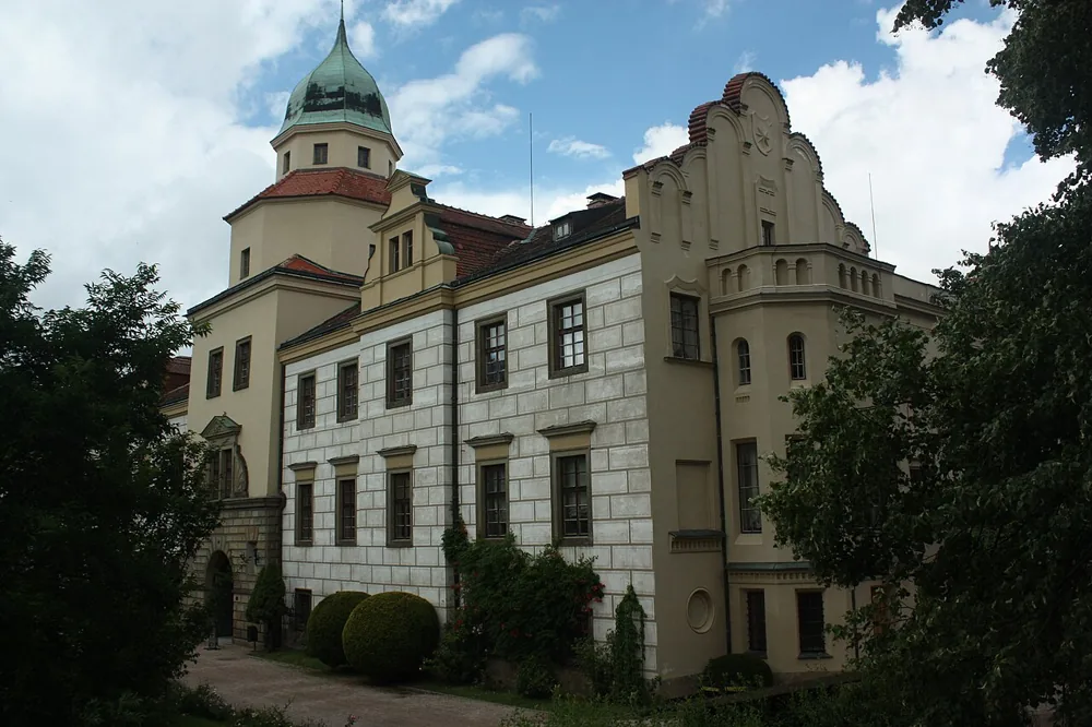 Světlé průčelí zámku Častolovice s vysokými okny, štíty a věží se zelenou střechou