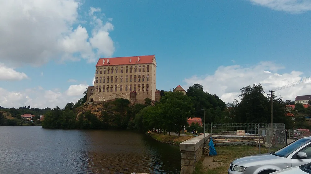 Vysoká budova zámku Plumlov na skalnatém návrší nad Podhradským rybníkem