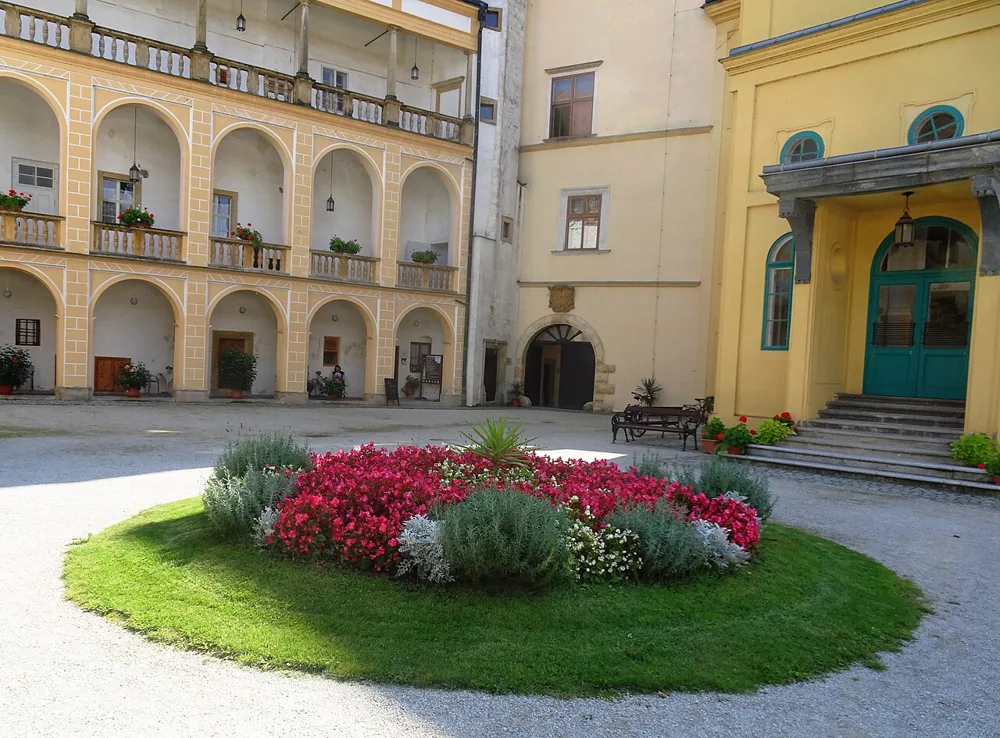 Nádvoří zámku Tovačov s arkádami, zelenými dveřmi a barevným květinovým záhonem