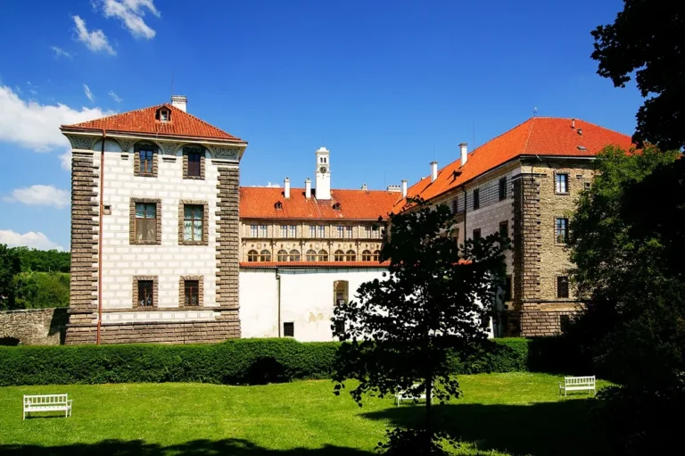 Renesanční křídla zámku Nelahozeves se zdobenou světlou fasádou a červenými střechami za zelenou plochou