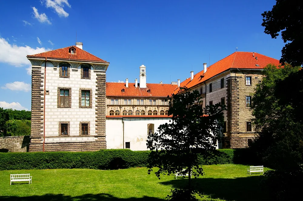 Renesanční křídla zámku Nelahozeves se zdobenou světlou fasádou a červenými střechami za zelenou plochou