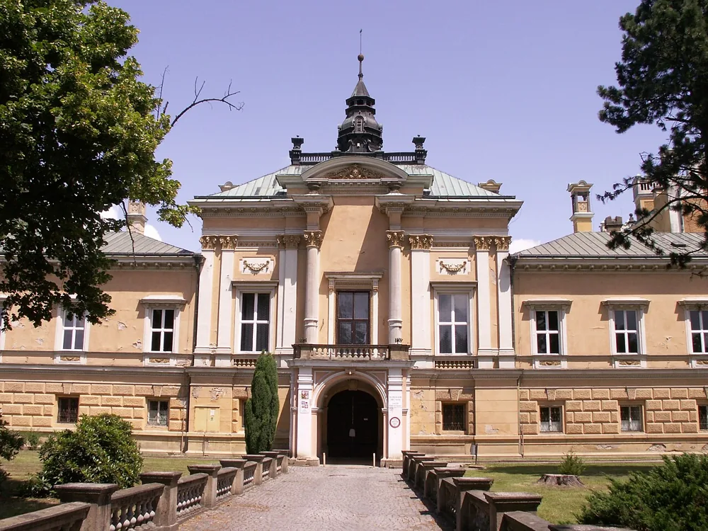 Světlé žluté průčelí zámku Světlá nad Sázavou se vstupem a věžičkou mezi stromy