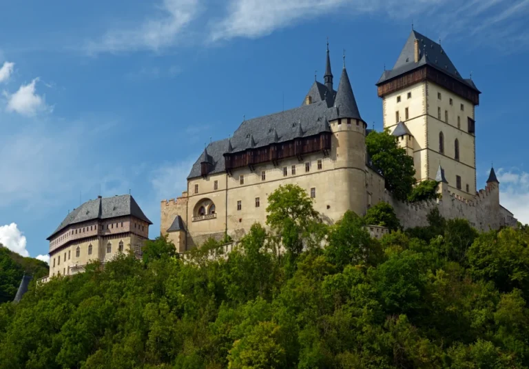 Hrad Karlštejn při pohledu od jihovýchodu, věže nad zalesněným svahem.