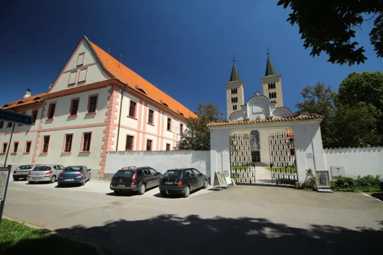 Vstupní brána milevského kláštera, historická budova vlevo a dvojice věží baziliky v pozadí.