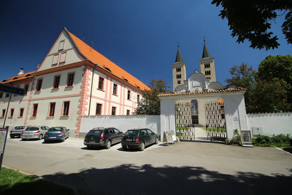 Vstupní brána milevského kláštera, historická budova vlevo a dvojice věží baziliky v pozadí.