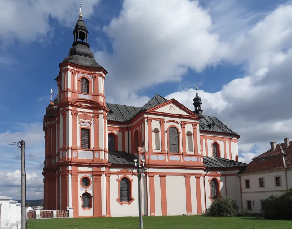 Barokní kostel Nanebevzetí Panny Marie v Přešticích s růžovobílou fasádou a věží.
