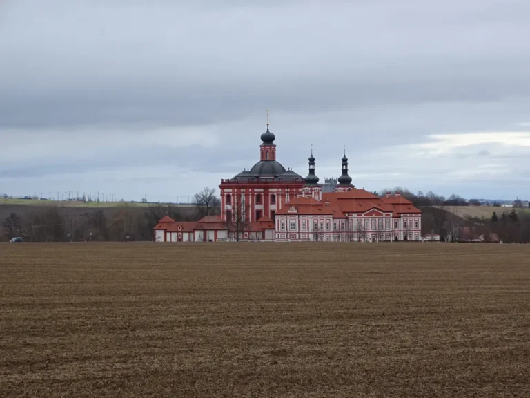 Červenobílý poutní areál Mariánské Týnice za polem pod zataženou oblohou.
