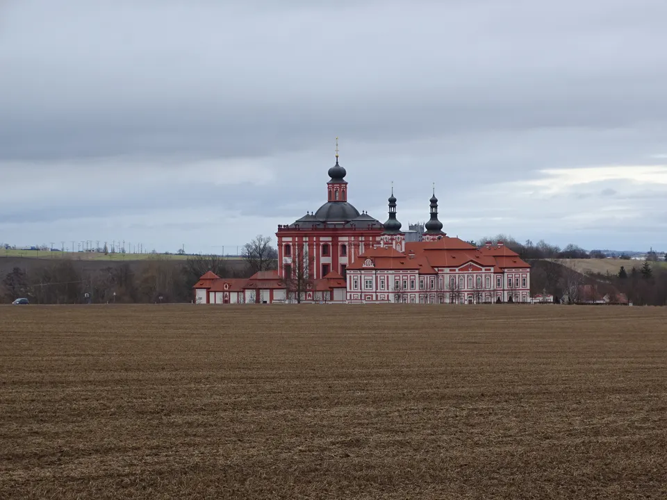Červenobílý poutní areál Mariánské Týnice za polem pod zataženou oblohou.