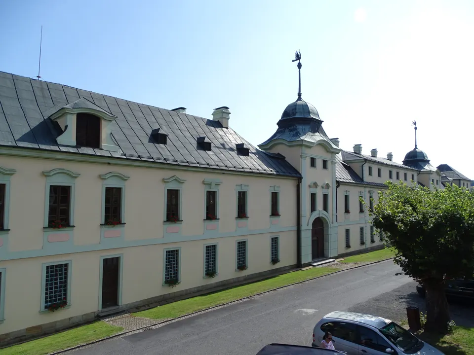 Dlouhé světlé průčelí zámku Manětín s věžičkami při pohledu z terasy náměstí.