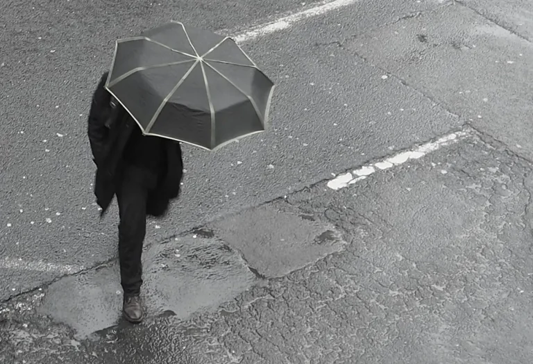 Člověk s deštníkem přecházející mokrou ulici